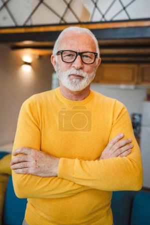 Téléchargez les photos : Un homme caucasien supérieur moderne portrait de grand-père masculin avec stand de barbe dans sa maison dans le chandail jaune usure de jour sérieux copie confiante espace portrait - en image libre de droit
