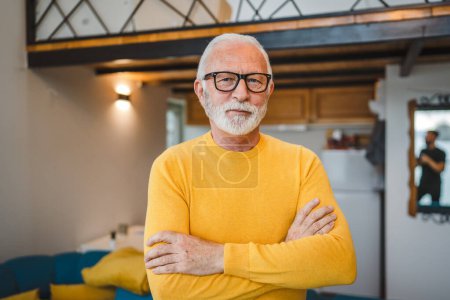 Téléchargez les photos : Un homme caucasien supérieur moderne portrait de grand-père masculin avec stand de barbe dans sa maison dans le chandail jaune usure de jour sérieux copie confiante espace portrait - en image libre de droit