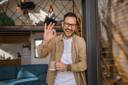 Photo for One man adult caucasian male with beard and eyeglasses stand on balcony at door in day happy smile hold cup of coffee copy space morning daily routine concept - Royalty Free Image