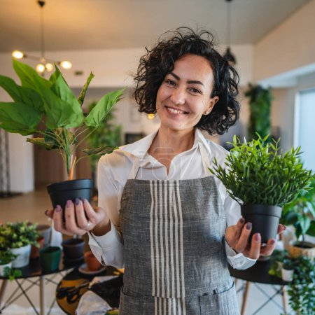 Téléchargez les photos : Une femme mature caucasienne femelle se tenir à la maison avec des plantes de fleurs pot heureux sourire tour de taille vue de face jardinage et botanique horticulture soins concept copier l'espace - en image libre de droit
