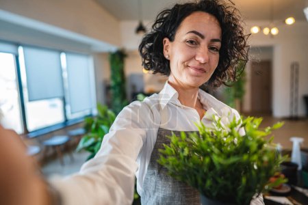Eine Frau reifen kaukasischen weiblichen Stand zu Hause mit Blumenpflanzen Topf glücklich lächeln Taille nach vorne Ansicht Garten und Botanik Gartenbau Pflegekonzept Selbstporträt Selfie UGC Benutzer generierte Inhalte