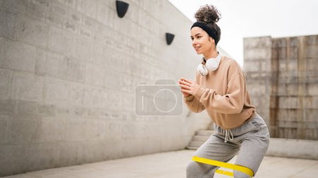 Foto de Una mujer adulta caucásica atleta entrenando con bandas elásticas de goma en exteriores en la ciudad sobre fondo de hormigón estirándose en feliz morena salud y fitness concepto de espacio de copia - Imagen libre de derechos