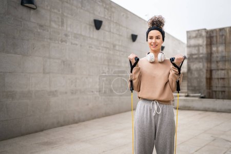 Téléchargez les photos : Une femme adulte caucasienne athlète entraînement féminin avec élastique bandes de résistance en caoutchouc tubes en plein air dans la ville sur fond de béton étirement dans heureux brune santé et fitness concept copier espace - en image libre de droit