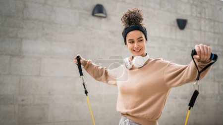 Photo for One woman adult caucasian female athlete training with elastic rubber resistance bands tubes outdoor in the city on concrete background stretching in happy brunette health and fitness concept copy space - Royalty Free Image