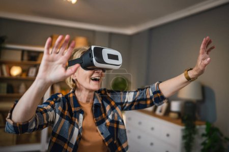 Foto de Una mujer madura senior caucásica hembra en casa disfrutar de realidad virtual VR auriculares - Imagen libre de derechos