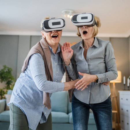 Foto de Dos mujeres maduras senior caucásico hembras viejo madre e hija en casa disfrutar de realidad virtual VR auriculares activo senior concepto copia espacio - Imagen libre de derechos