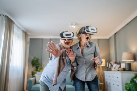 Foto de Dos mujeres maduras senior caucásico hembras viejo madre e hija en casa disfrutar de realidad virtual VR auriculares activo senior concepto copia espacio - Imagen libre de derechos