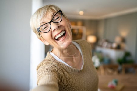 Foto de Primer plano retrato de una mujer mayor con el pelo corto sonrisa feliz emoción positiva copia espacio de pie en casa gafas de desgaste interior auto retrato ugc usuario generado contenido - Imagen libre de derechos
