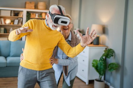 Photo for Man mature senior caucasian male husband with his wife senior couple at home enjoy virtual reality VR headset - Royalty Free Image