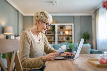 Photo for One mature senior woman grandmother sit at home use credit or debit card for online shopping browse internet stores use laptop computer buying stuff real people copy space - Royalty Free Image