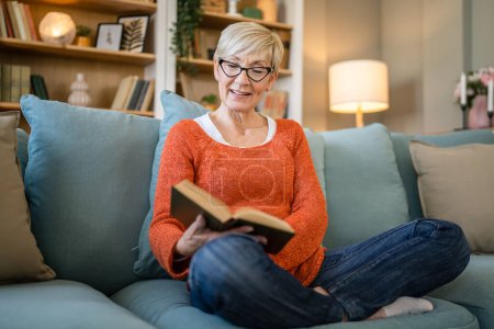 Foto de Una mujer madura mayor caucásica pensionista moderna abuela con pelo corto leer libro en casa gafas de desgaste espacio de copia en persona real - Imagen libre de derechos