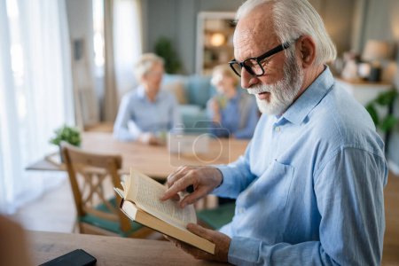 Téléchargez les photos : Un homme mature homme caucasien âgé pensionné grand-père moderne avec les cheveux courts et la barbe lire le livre à la maison porter des lunettes espace de copie personne réelle - en image libre de droit