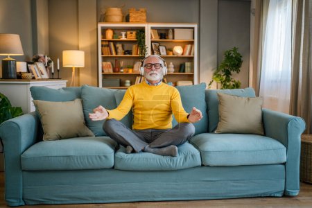 Foto de Un hombre adulto mayor caucásico masculino usando auriculares para la meditación guiada en línea practicando mindfulness manifestación de yoga con los ojos cerrados en casa personas reales autocuidado concepto copia espacio - Imagen libre de derechos