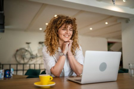 Photo for One woman adult caucasian female with curly hair work on laptop computer while sit at cafe real person copy space happy smile confident - Royalty Free Image