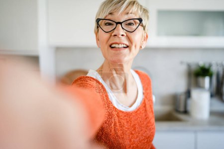 Téléchargez les photos : Gros plan portrait d'une femme âgée aux cheveux courts heureux sourire positif émotion copie espace debout à la maison dans la cuisine intérieur lunettes autoportrait ugc utilisateur généré contenu - en image libre de droit