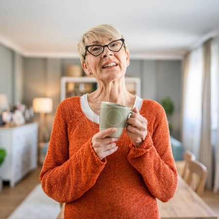 Téléchargez les photos : Portrait rapproché d'une femme âgée aux cheveux courts sourire heureux espace de copie d'émotion positive debout à la maison lunettes de vue portent une tasse de café routine quotidienne du matin - en image libre de droit