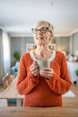 Téléchargez les photos : Portrait rapproché d'une femme âgée aux cheveux courts sourire heureux espace de copie d'émotion positive debout à la maison lunettes de vue portent une tasse de café routine quotidienne du matin - en image libre de droit