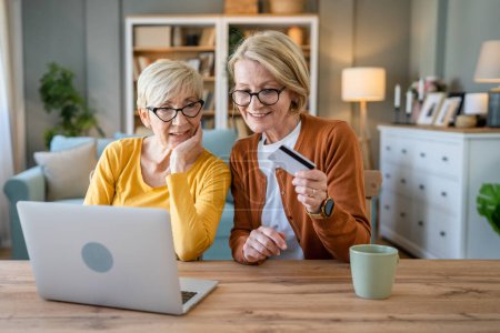 Photo for Two mature senior women grandmother females sit at home use credit or debit card for online shopping browse internet stores buying stuff use digital tablet real people copy space - Royalty Free Image