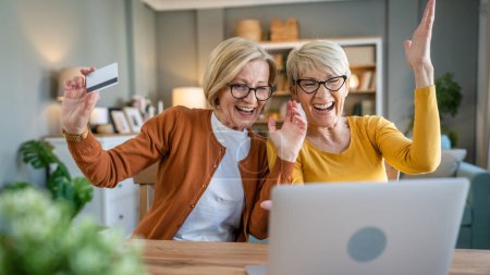 Photo for Two mature senior women grandmother females sit at home use credit or debit card for online shopping browse internet stores buying stuff use digital tablet real people copy space - Royalty Free Image
