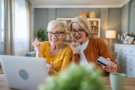 Téléchargez les photos : Deux femmes âgées matures grand-mère femelles assis à la maison utiliser carte de crédit ou de débit pour les achats en ligne parcourir les magasins en ligne acheter des trucs utiliser tablette numérique personnes réelles copier l'espace - en image libre de droit