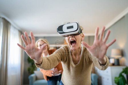 Téléchargez les photos : Deux femmes âgées matures caucasiennes amies ou sœurs à la maison profiter de la réalité virtuelle VR casque vraies personnes âgées actives ayant plaisir concept de loisirs - en image libre de droit