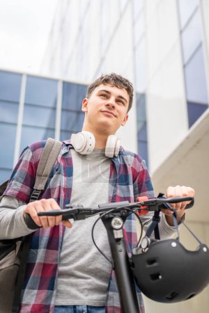 Téléchargez les photos : Un jeune homme caucasien adolescent homme génération Z avec coup de pied électrique pousser scooter au bâtiment moderne dans la ville éco mode de transport concept copier l'espace - en image libre de droit
