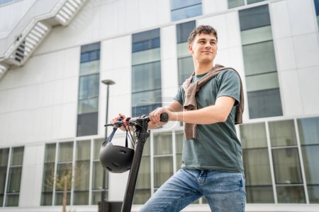 Téléchargez les photos : Un jeune homme caucasien adolescent homme génération Z avec coup de pied électrique pousser scooter au bâtiment moderne dans la ville éco mode de transport concept copier l'espace - en image libre de droit