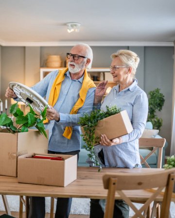 Photo for Family senior couple man woman husband and wife pensioner grandfather grandmother moving in new apartment taking their stuff belongings and plants in or out of boxes packing or unpacking real people - Royalty Free Image