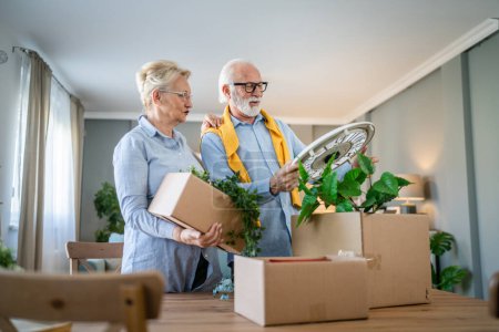 Photo for Family senior couple man woman husband and wife pensioner grandfather grandmother moving in new apartment taking their stuff belongings and plants in or out of boxes packing or unpacking real people - Royalty Free Image