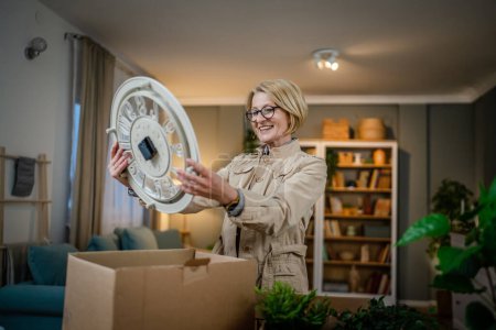 Photo for One senior woman pensioner grandmother moving in new apartment taking her stuff belongings and plants in or out of boxes packing or unpacking real person copy space - Royalty Free Image