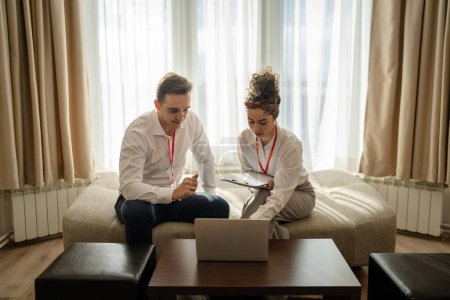 Photo for Two people man and woman colleagues sitting together at hotel room with contracts and documents preparing for sales meeting or conference making plans sharing experience real people business concept - Royalty Free Image
