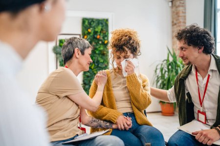 Un grupo de personas sentadas en un círculo con dos terapeutas y una mujer en el centro discutiendo y brindando apoyo emocional para ella.
