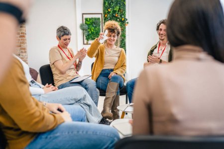 Photo for A group of people sitting in a circle with two therapists and a woman in the center discussing and providing emotional support for her The focus is on the woman but everyone is engaged in conversation - Royalty Free Image