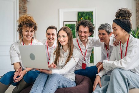 Téléchargez les photos : Un groupe de professionnels masculins et féminins portant des chemises blanches sont assis avec une jeune femme tenant un ordinateur portable et d'autres regardant un projet heureux et sourire travailler ensemble heureux - en image libre de droit