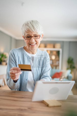Photo for One mature senior woman grandmother sit at home use credit or debit card for online shopping browse internet stores buying stuff real people copy space - Royalty Free Image