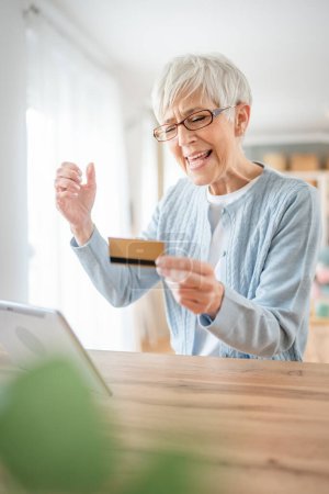 Photo for One mature senior woman grandmother sit at home use credit or debit card for online shopping browse internet stores buying stuff real people copy space - Royalty Free Image