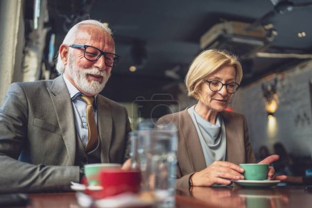 Foto de Mujer madura y una pareja de hombres mayores participan en la conversación, mientras que tienen una taza de calor de café y camaradería saborear el simple placer de buena compañía creando recuerdos en el entorno de la cafetería - Imagen libre de derechos