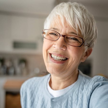 Téléchargez les photos : Gros plan portrait d'une femme âgée aux cheveux courts heureux sourire positif émotion copie espace debout à la maison intérieur gris cheveux blancs autoportrait selfie ou appel vidéo - en image libre de droit