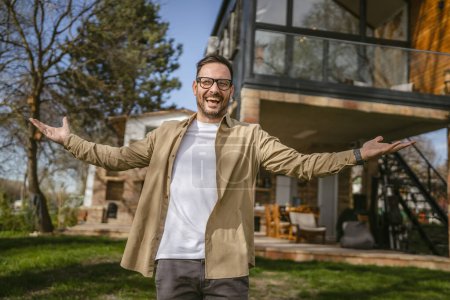 Téléchargez les photos : Un homme caucasien adulte moderne portrait d'homme avec barbe et lunettes se tiennent devant sa maison dans l'espace de copie confiant heureux jour - en image libre de droit