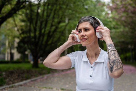 Photo for One woman mature caucasian senior female sit outdoor with headphones for guided meditation prepare to meditate front view real people self-care manifestation practice mental emotional balance concept - Royalty Free Image