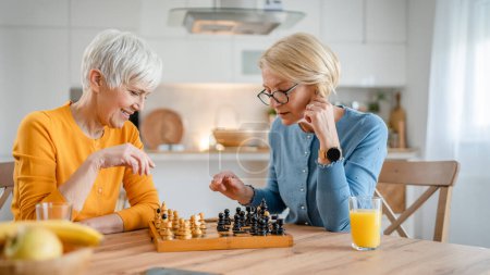 Téléchargez les photos : Deux femmes âgées matures caucasiennes femmes amies ou sœurs jouent jeu d'échiquier de loisirs à la maison avoir du plaisir passer du temps ensemble à la maison lumineux espace de copie de photos - en image libre de droit