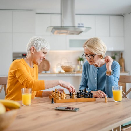 Foto de Dos mayores mujeres maduras caucásicas mujeres amigas o hermanas juegan al ajedrez de ocio juego de mesa en casa divertirse pasar tiempo juntos en casa brillante fotocopia espacio - Imagen libre de derechos