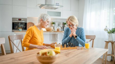 Foto de Dos mayores mujeres maduras caucásicas mujeres amigas o hermanas juegan al ajedrez de ocio juego de mesa en casa divertirse pasar tiempo juntos en casa brillante fotocopia espacio - Imagen libre de derechos