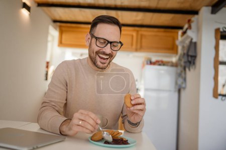 Photo for One adult man caucasian old male sit at a table at home putting jam on a biscuit preparing to eat breakfast enjoy snack relaxed in his home environment real person copy space daily routine - Royalty Free Image
