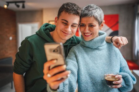 Foto de Adolescente chico joven hombre y madura mujer madre e hijo tomar selfie fotos autorretratos en casa - Imagen libre de derechos