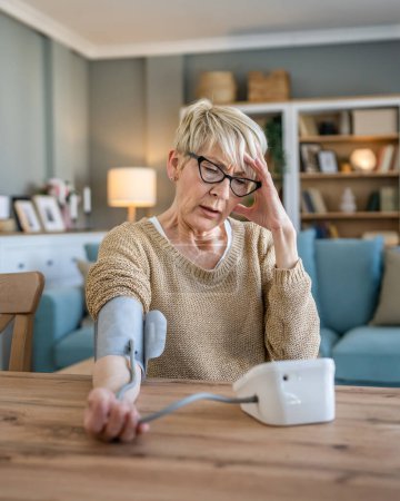 Foto de Una mujer mayor caucásica hembra utilizar el dispositivo de presión arterial en la mano para comprobar los resultados de salud mientras se sienta en casa personas reales concepto de atención de la salud - Imagen libre de derechos