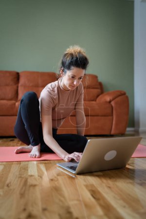 Photo for One woman adult caucasian female sitting on the training mat at home using laptop computer to browse internet for online guided training course real people self care concept copy space - Royalty Free Image