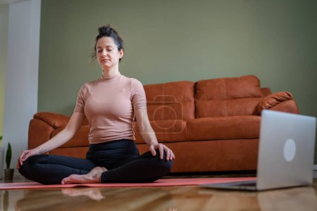 Foto de One woman adult caucasian female millennial practice online guided meditation use laptop for practicing mindfulness yoga with eyes closed on the floor at home real people self care concept copy space - Imagen libre de derechos