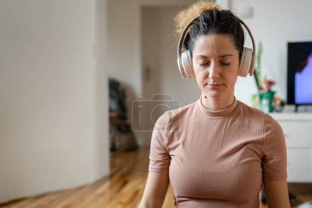 Foto de Una mujer adulta caucásica milenaria usando auriculares para meditación guiada en línea practicando mindfulness yoga con los ojos cerrados en el suelo en casa personas reales autocuidado concepto de espacio de copia - Imagen libre de derechos
