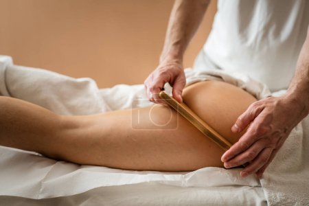 Photo for Unknown Caucasian woman having madero therapy massage anti-cellulite treatment by professional therapist holding wooden tools in hands in studio or salon with copy space - Royalty Free Image